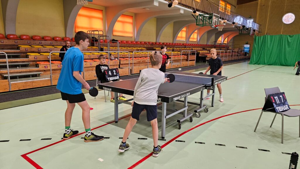 Młodzież gra w tenisa stołowego w hali sportowej