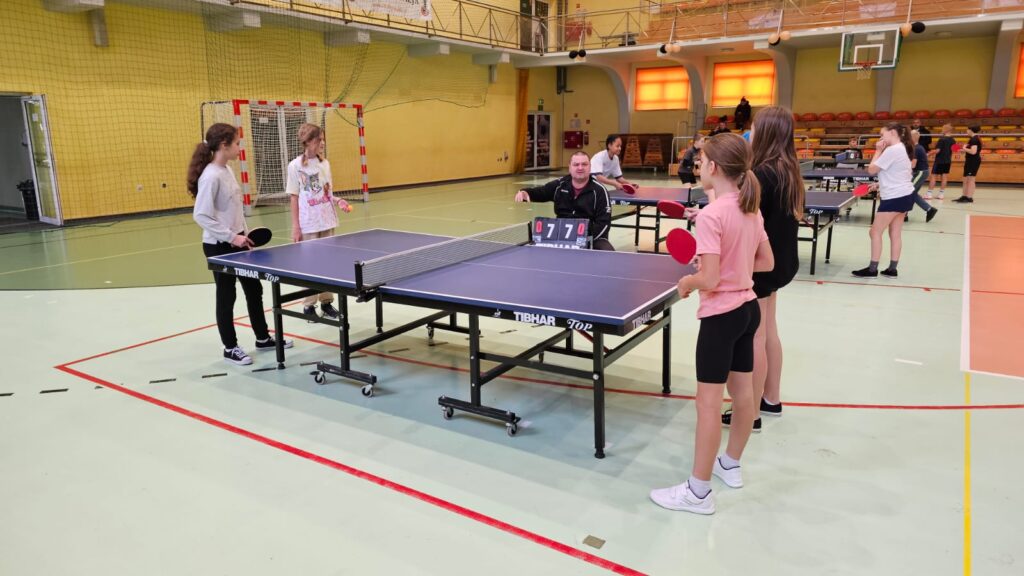 Młodzież gra w tenisa stołowego w hali sportowej